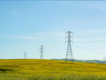 High-tension lines cut across rolling hills, weaving a modern energy network amidst the natural landscape.